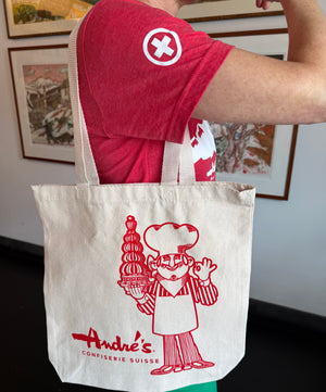 Person wearing a red shirt with a logo, holding a white tote bag with red graphics and text.