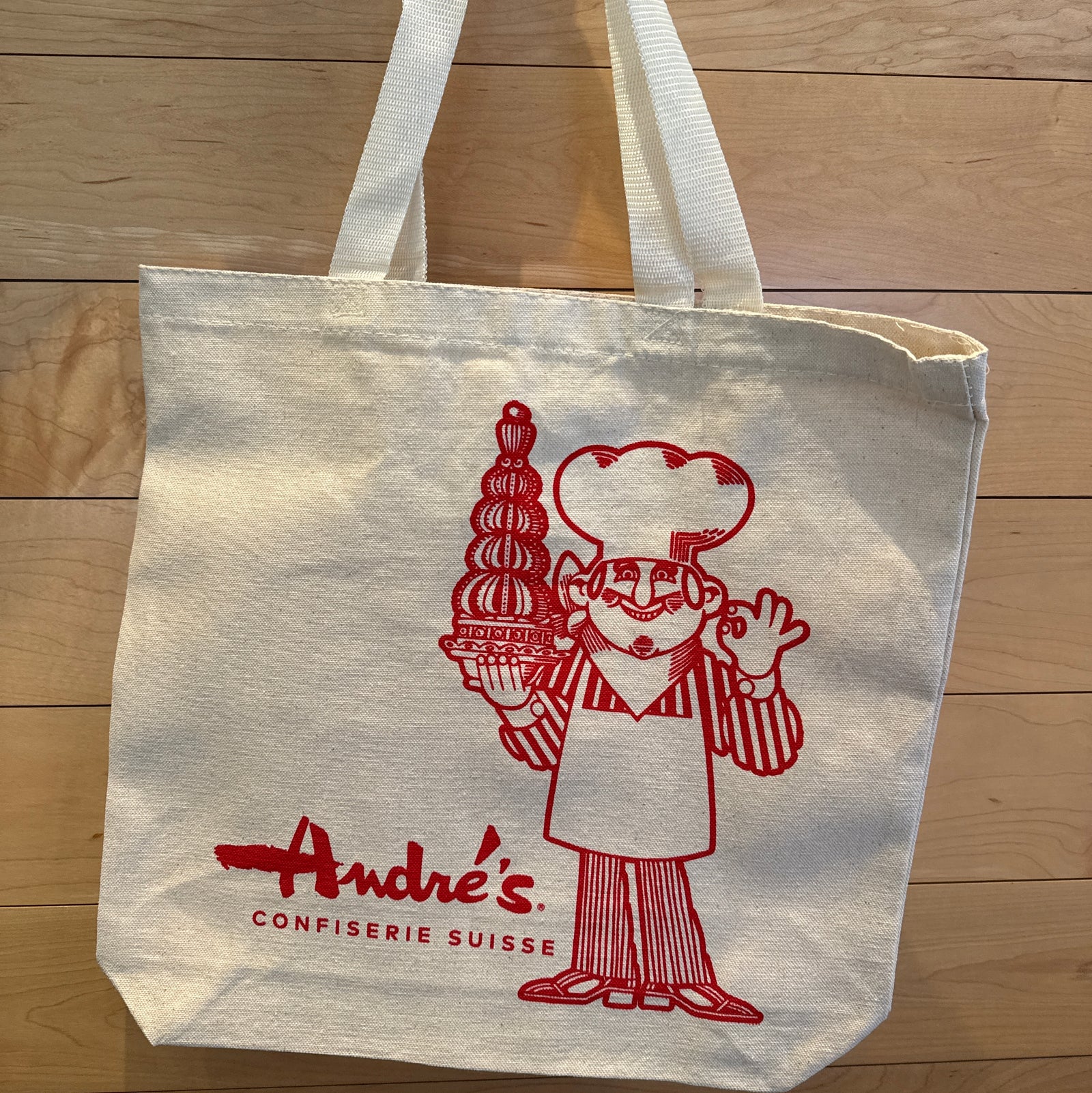 Tote bag with red logo and text on a wooden surface