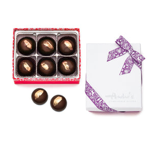 6 dark chocolate round truffles with gold brushstroke design on top in a red box, 2 loose chocolates, and the closed box with white "Andre's" logo lid and lavender Swiss print ribbon