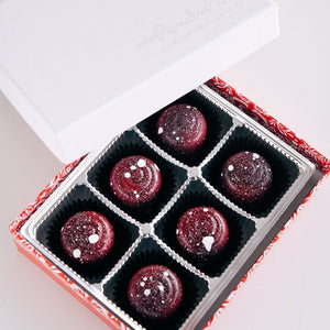open box of chocolates with a white lid askew showing six carefully placed red and white decorated bonbon chocolate inside a red box with six dividers on a plain white background