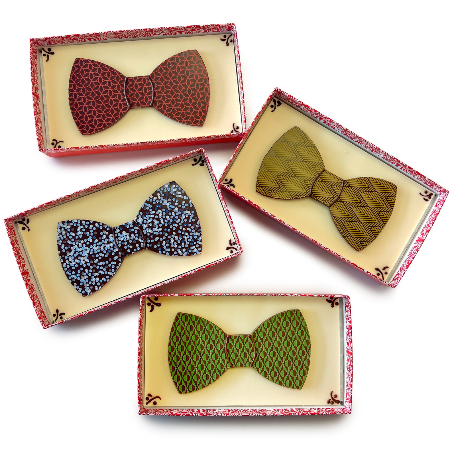 4 brightly colored flat chocolate bow ties on white chocolate bases in boxes without lids.
