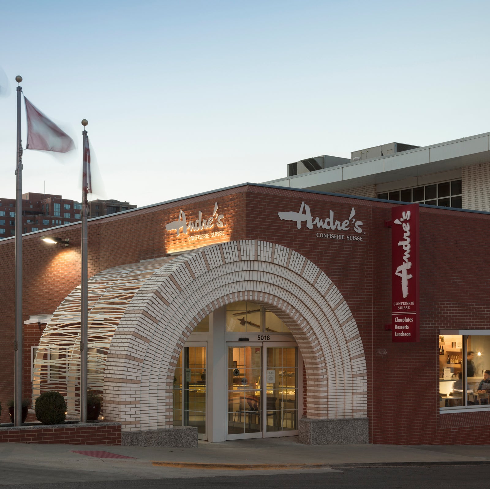Exterior of Main Street KC Andre's location with flagpoles, white brick arch, and logo signs.