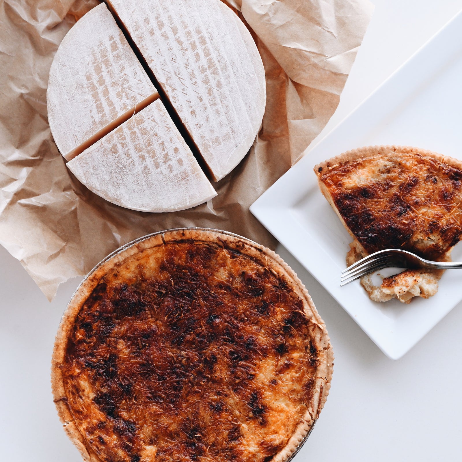 overhead view of full Alpine Quiche, slice, and wheel of cheese.
