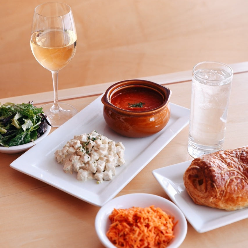 Salads, soup and croissant plated with glasses of water and wine.