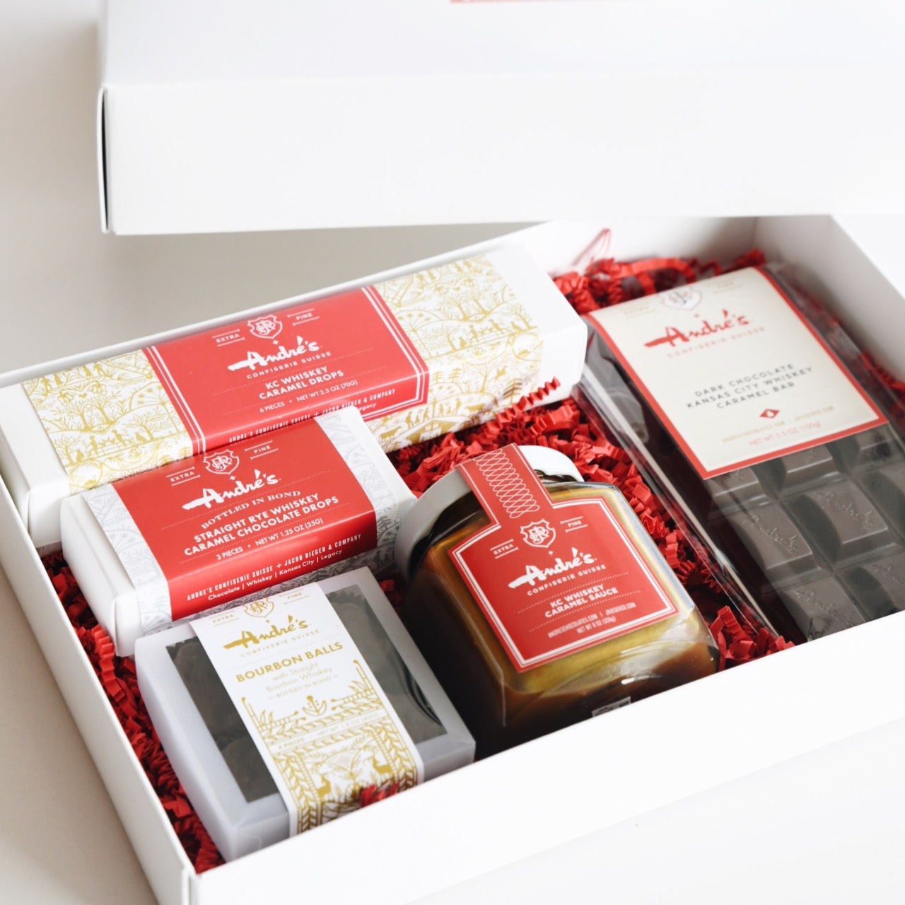 White table and open white box with contents of the Rieger Whiskey Chocolate Gift Box nestled with red springfill.