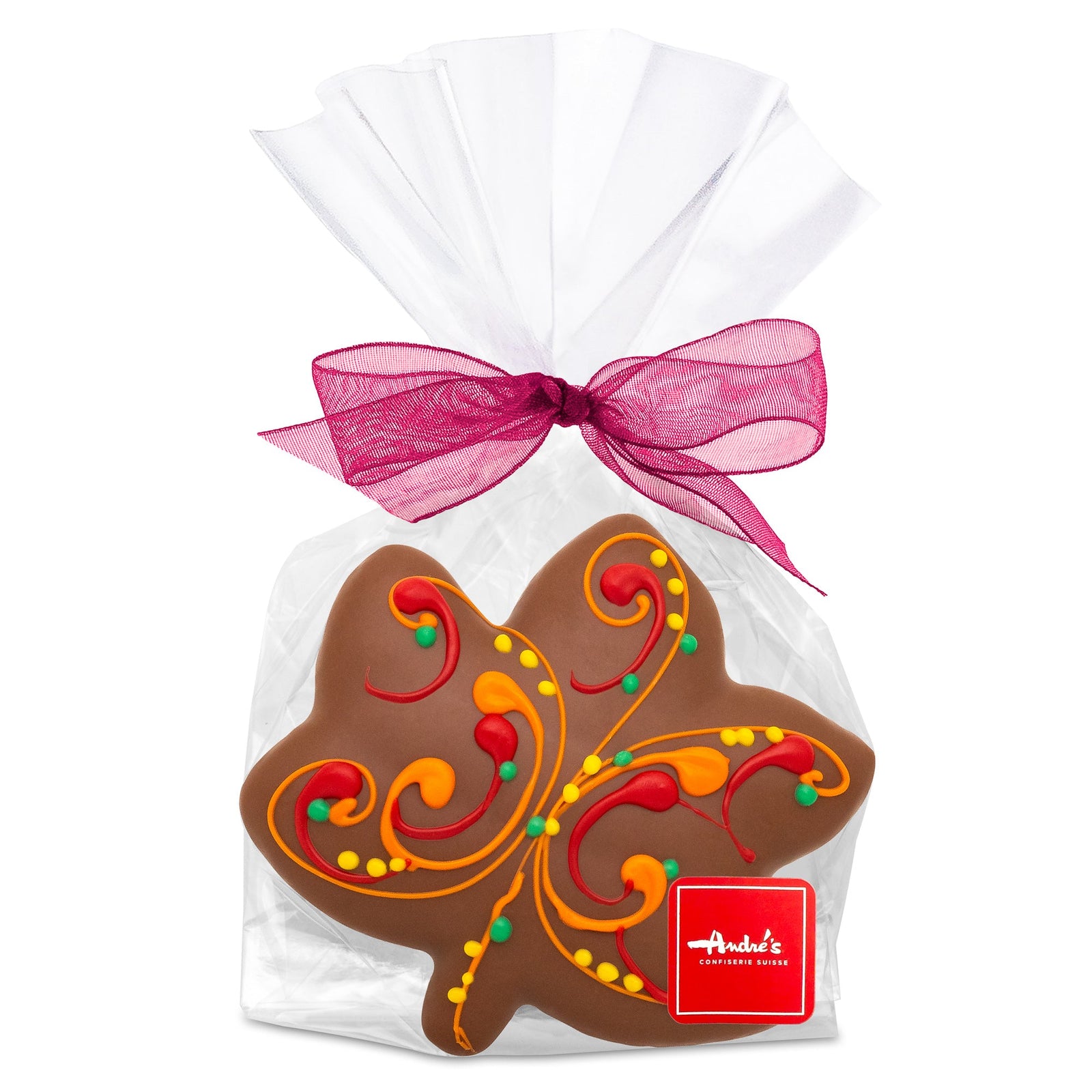 A maple leaf-shaped gingerbread cookie, covered in dark chocolate and decorated with bright fall color dots, in a clear bag with an orange bow and red Andre's logo sticker.