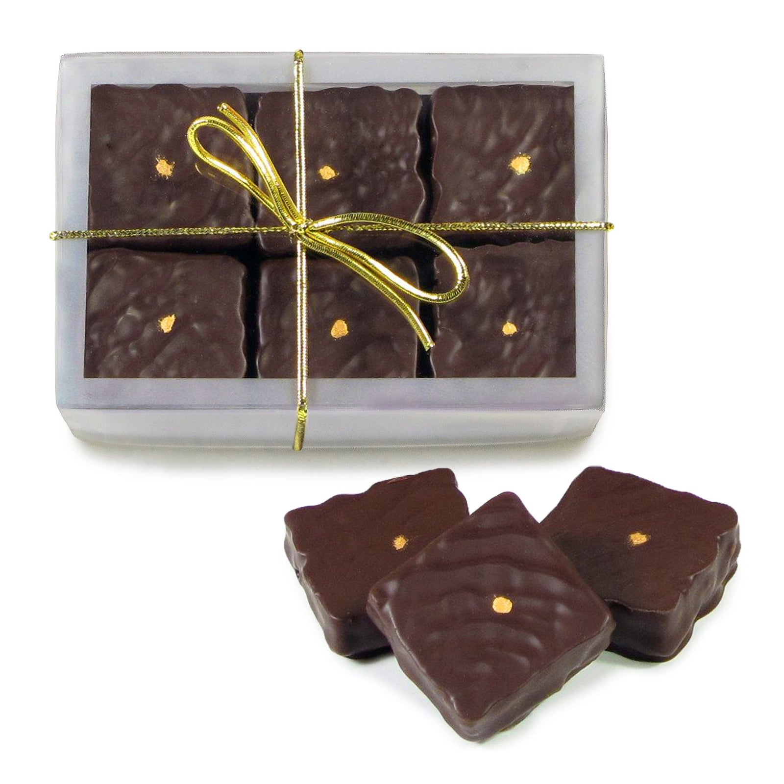 Rectangular clear box containing dark chocolate square candies that have small gold dots in each center with 3 candies loose beside. A gold stribbon bow is wrapped around the box.