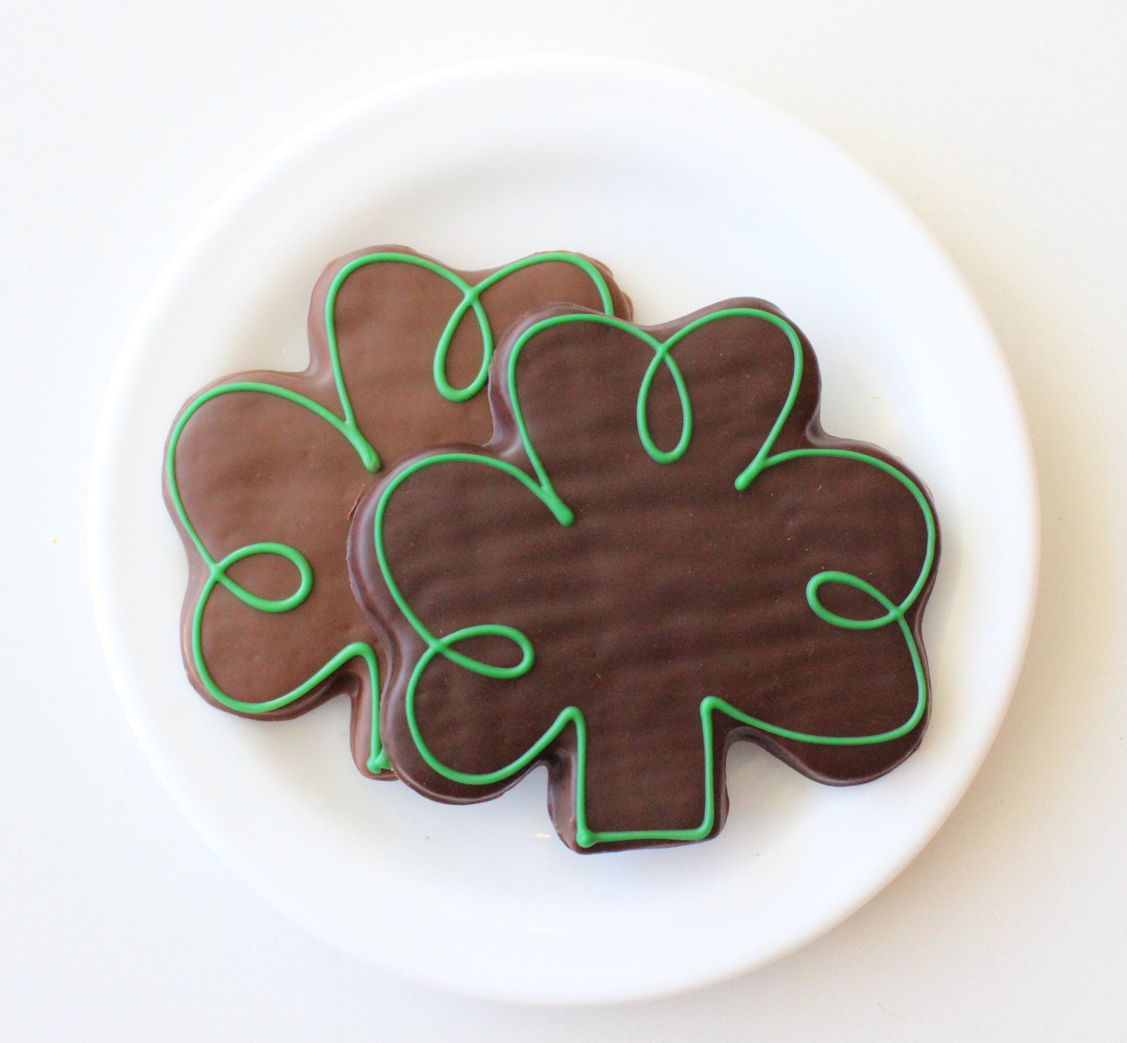 A clover leaf-shaped cookie, covered in milk chocolate and decorated with green swirls, in a clear bag with a green bow and Andre's logo sticker.