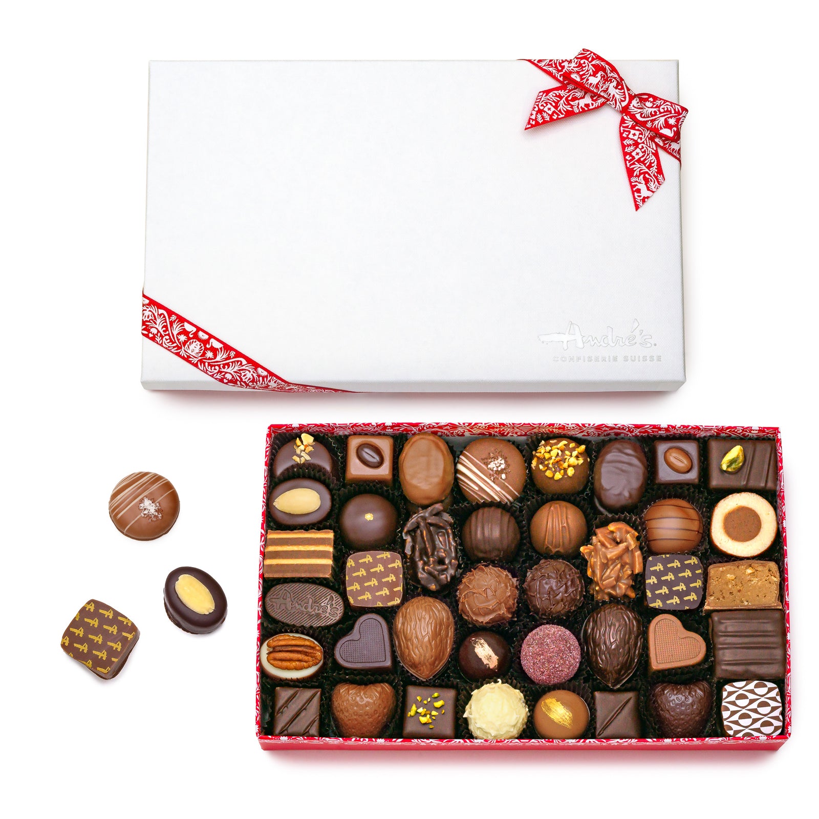 A red box base filled with 40 assorted chocolate candies next to its white Andre's logo lid and red Swiss patterned bow. 3 loose candies beside it.