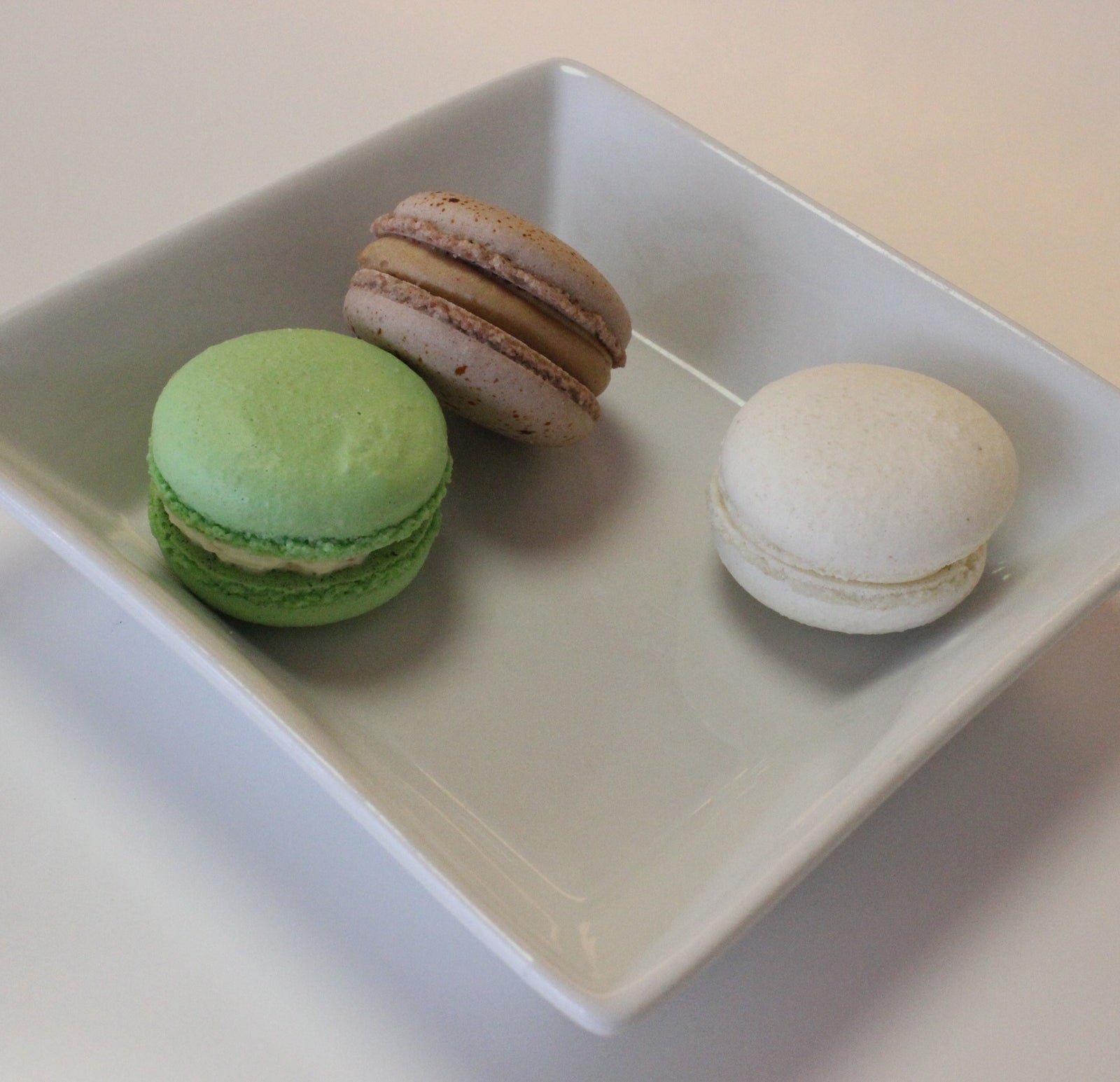 Rows of luxemburgerli cookies: white with vanilla cream center, green with chocolate cream center, speckled tan with caramel cream center.