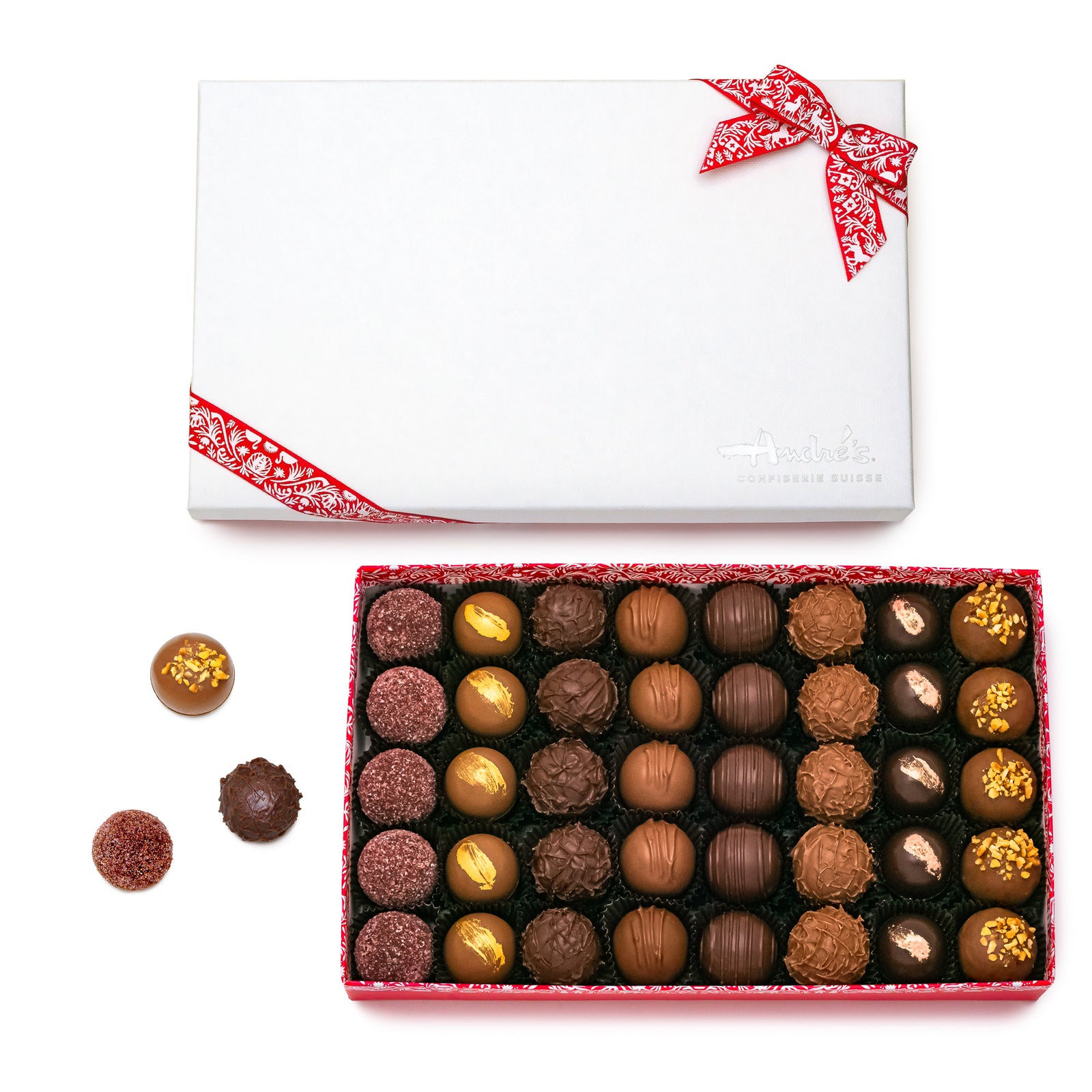 A box of assorted chocolate truffles with a white box wrapped in red ribbon, the truffles vary in color and are topped with different ingredients.