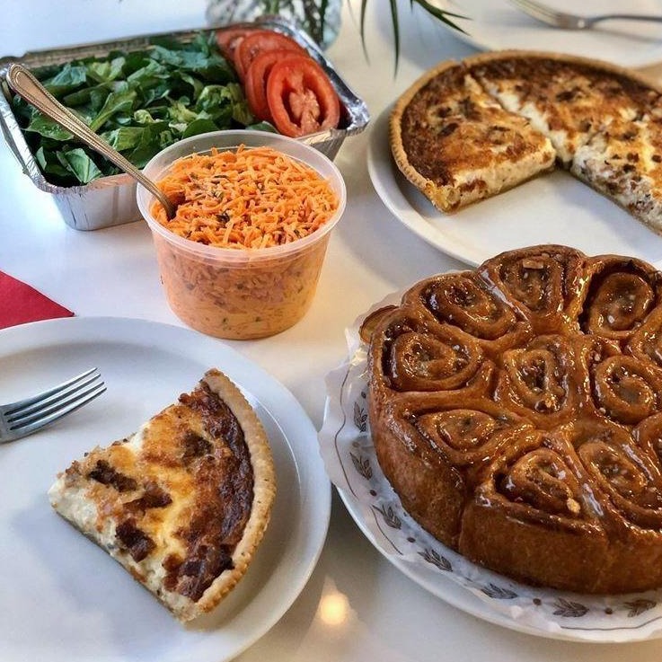 A variety of prepared foods on a table, including two salads, a quiche, and a coffee cake.
