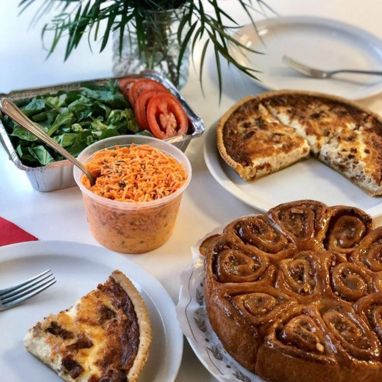 A variety of prepared foods including two salads, a quiche, and coffee cake, arranged on a table for a family brunch.