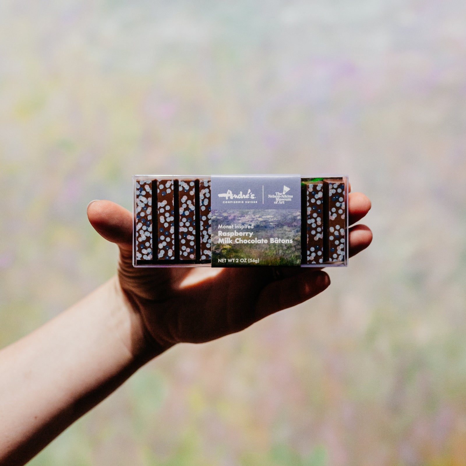 A clear box filled with milk chocolate sticks that have blue circle designs, wrapped with a product label showing Monet's Water Lilies artwork.