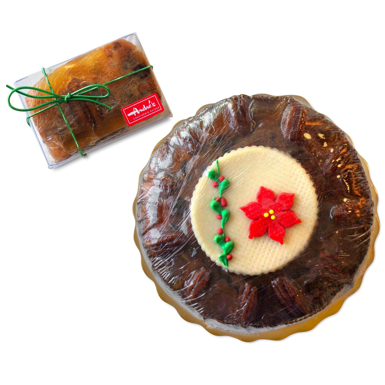 A round fruitcake with visible pecans around the edge on a gold scalloped base and round white candy disk that has candy holly and poinsettia next to a square fruitcake in a rectangular box.