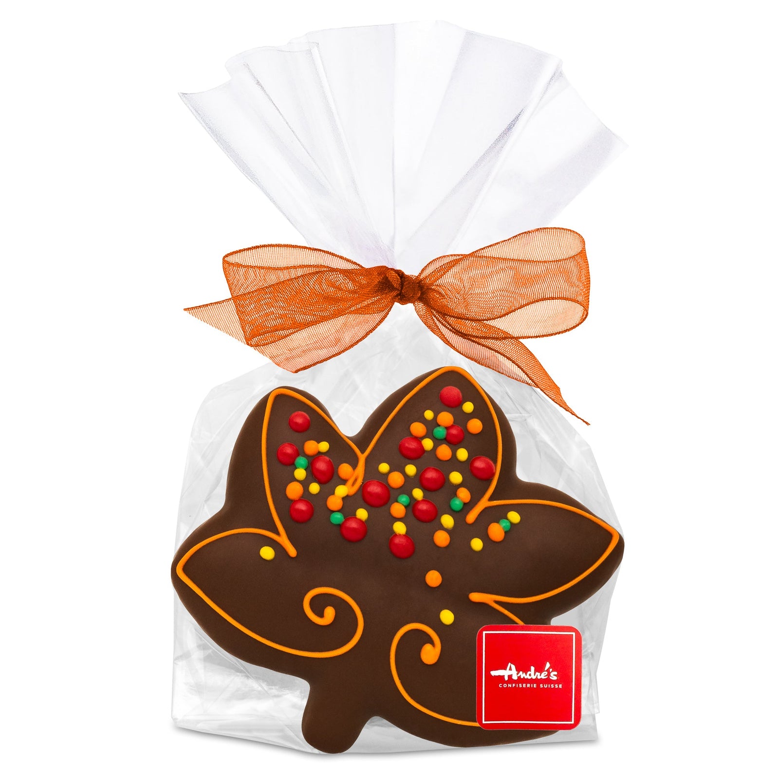 A maple leaf-shaped gingerbread cookie, covered in dark chocolate and decorated with bright fall color dots, in a clear bag with an orange bow and red Andre's logo sticker.
